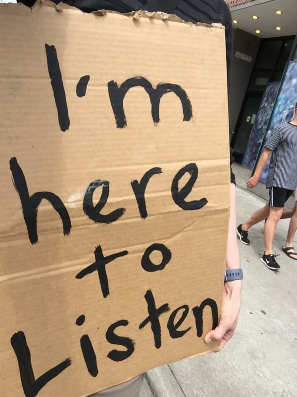 holding a sign in a protest march that says "I'm here to listen"